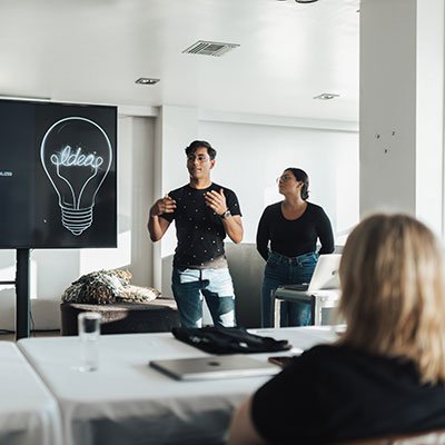 Two trainers presenting in a training session for automotive industry professionals, with a focus on enhancing sales performance and operational efficiency, featuring a light bulb graphic labeled "Ideas."