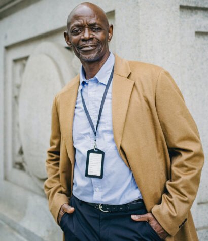 Professional man in a tan coat and blue shirt, smiling confidently, representing the expertise of Solo Performance LLC's leadership team in automotive training and consulting.