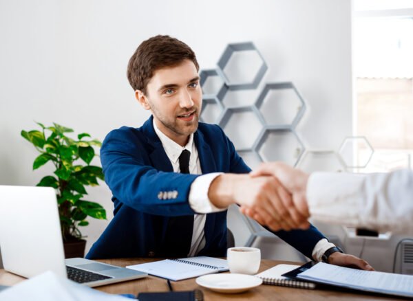 Sales Associate to Top Performe Young businessman shaking hands in an office setting, symbolizing partnership and collaboration in automotive sales.