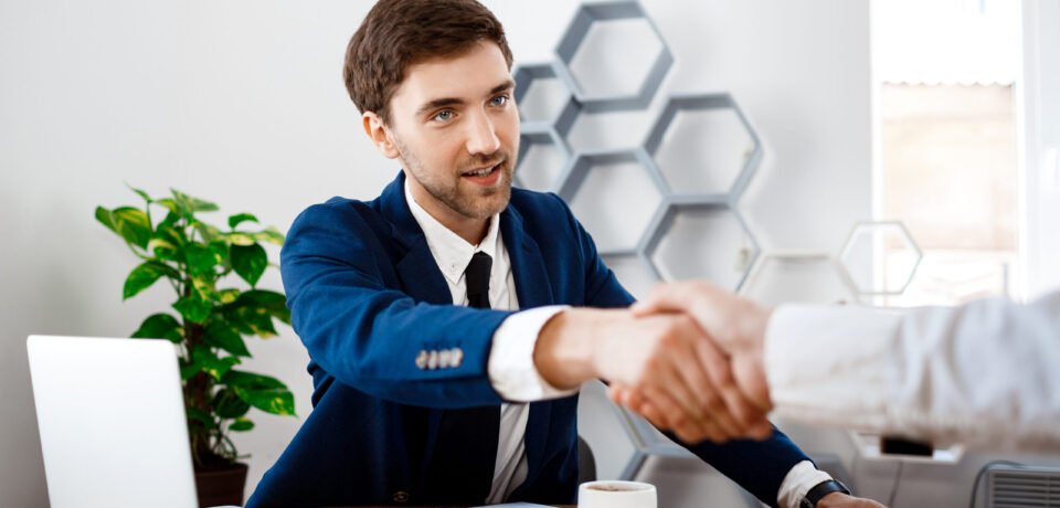 Young businessman in a blue suit shaking hands in a modern office setting, symbolizing successful business consulting and partnership.